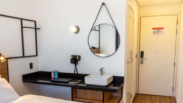A hotel room with a bed, a desk with a sink, a mirror, a phone, and a door.