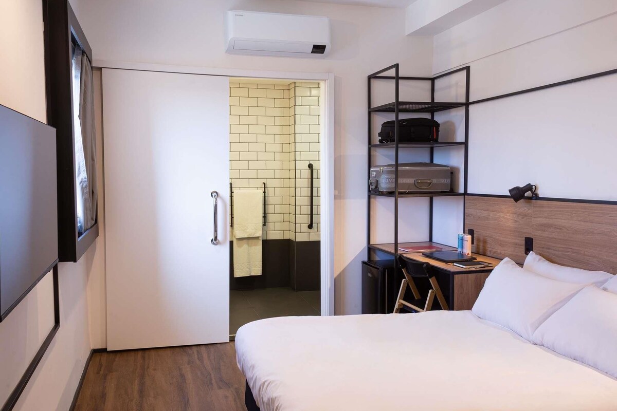 A hotel room with a bed, a desk, a chair, a TV, and a wardrobe.