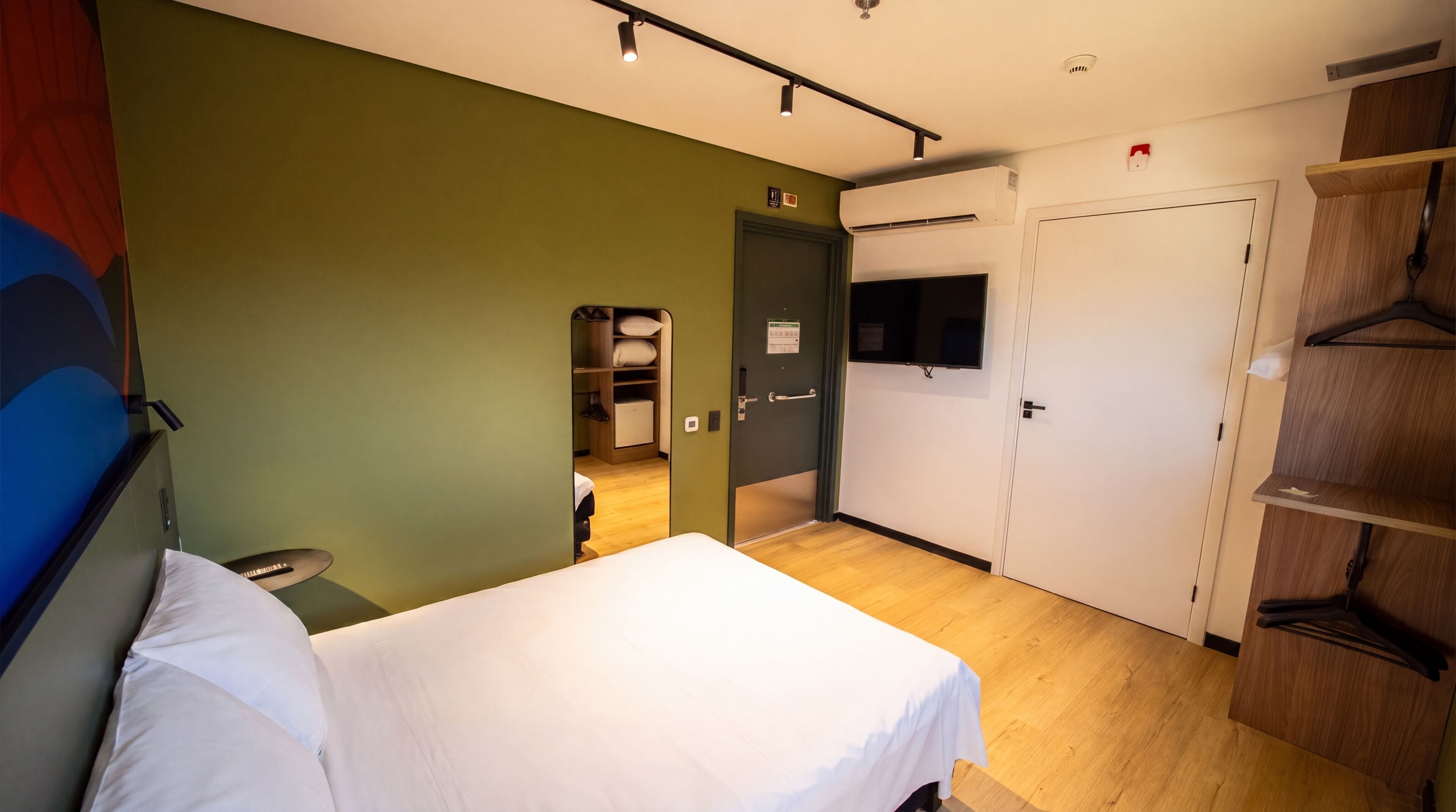 Une chambre d’hôtel avec un lit, une armoire, un miroir et un téléviseur.