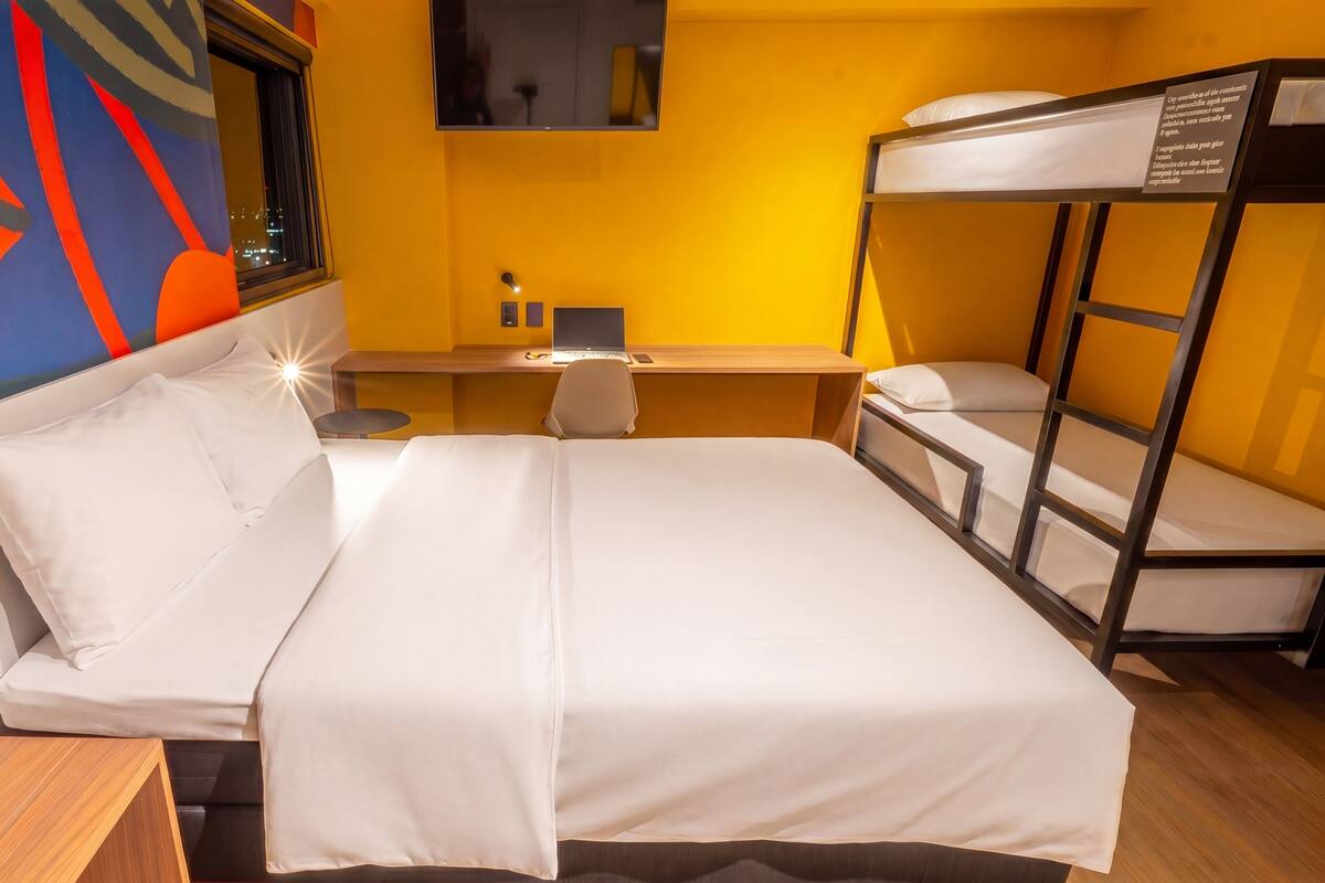 A hotel room with a bed, desk, and bunk beds.