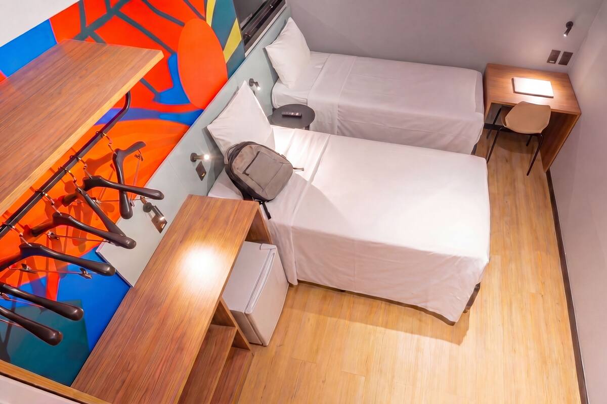 A compact hotel room with a bed, a desk, a chair, a small table, and a TV.