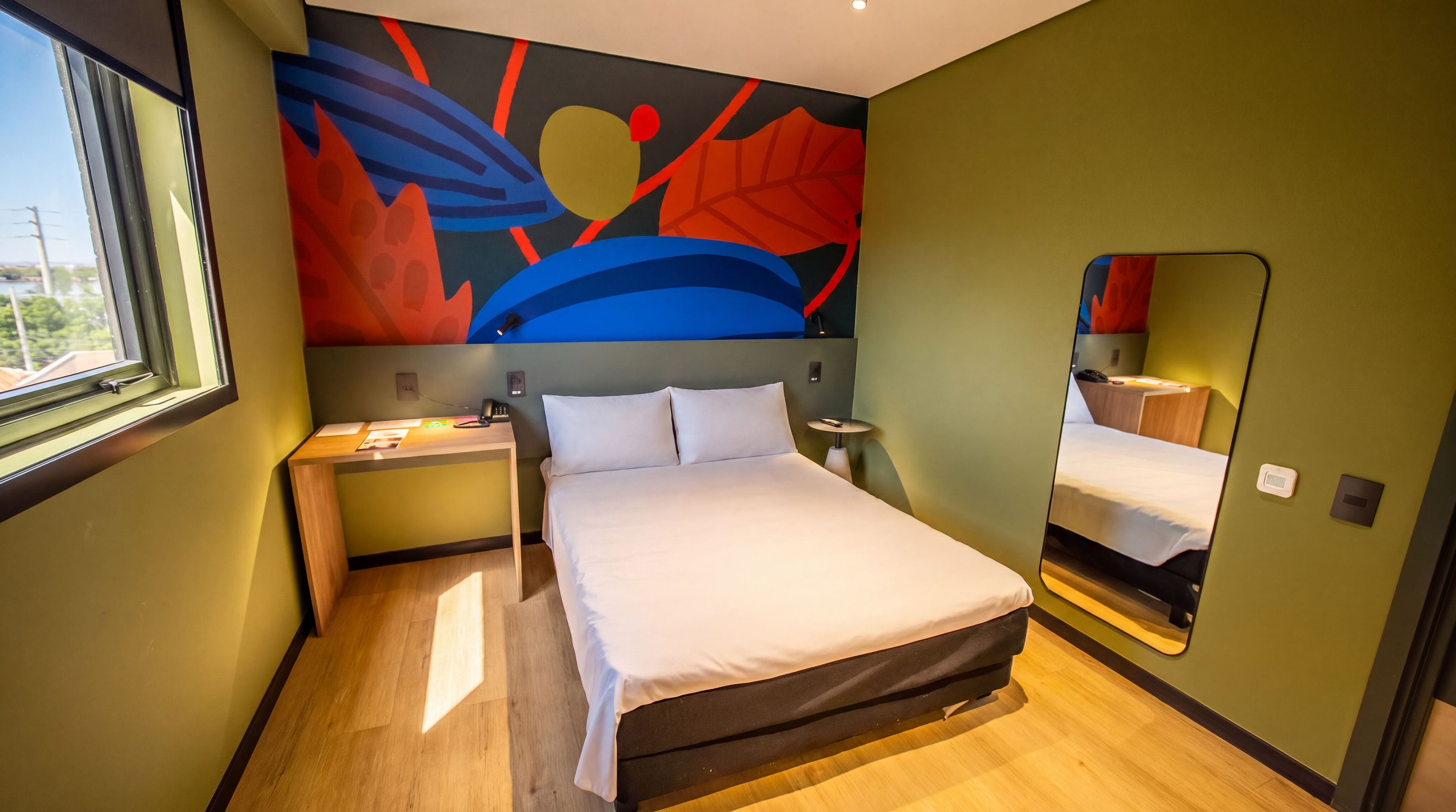 Een hotelkamer met een bed, nachtkastje en een groot abstract schilderij aan de muur.