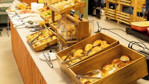 Ein Buffet mit verschiedenen Speisen in Holzbehältern, eine Wand mit Frucht- und Gemüse-Mustern und ein grünes Ausgangsschild.