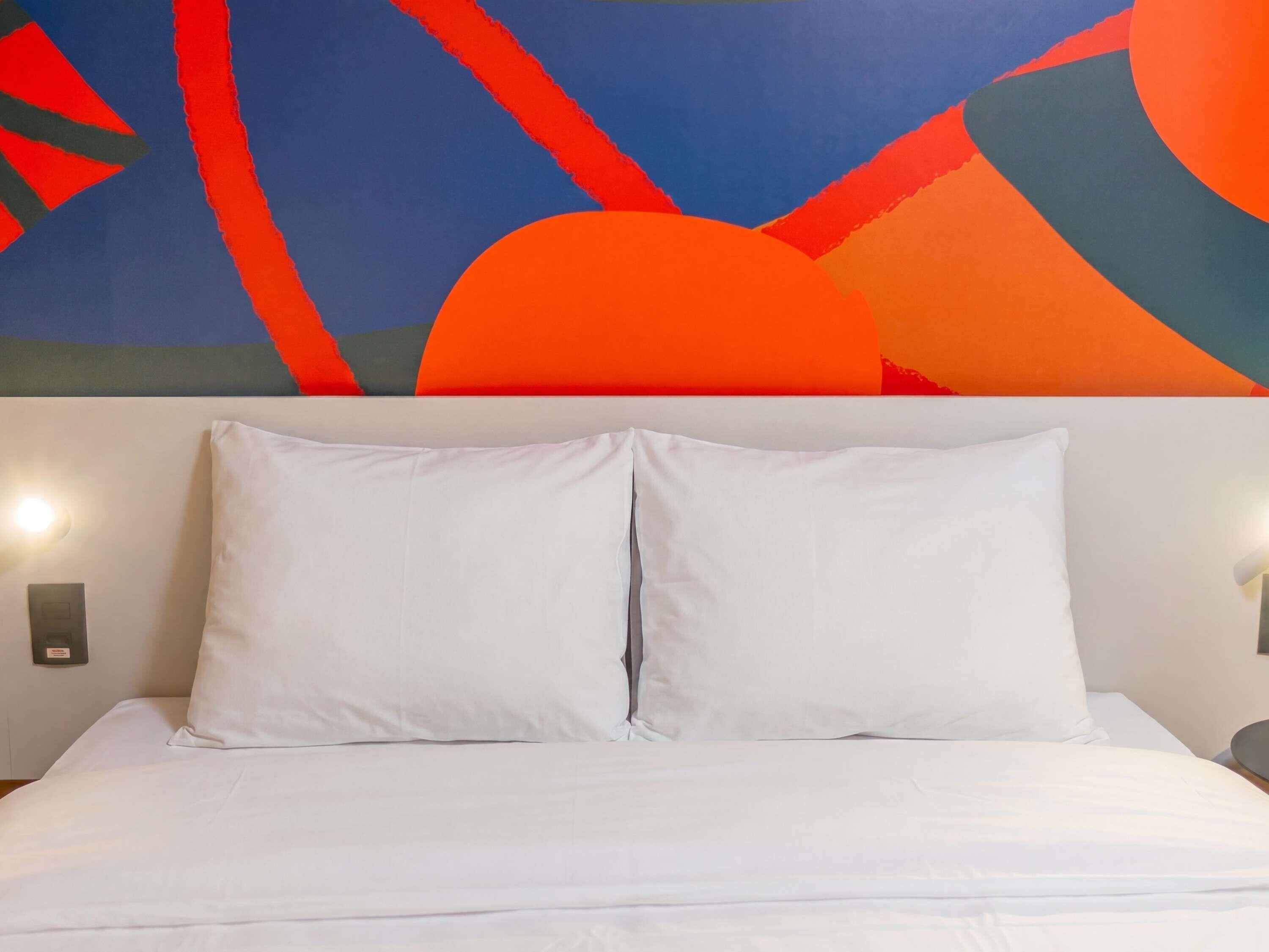 A bed with white bedding, a plain headboard, and two wall-mounted light fixtures.