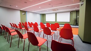 Une salle de conférence avec des rangées de chaises rouges, un écran de projection et une moquette verte.