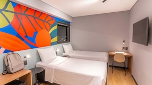 Habitación de hotel con dos camas, un escritorio, una silla, un televisor y un mural de pared colorido.