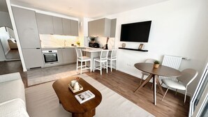 En moderne opholdsstue med et køkken, spiseplads og siddeområde med sofabord.