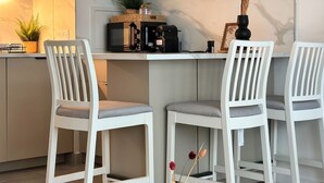 Et moderne køkken med hvide skabe, en kaffemaskine og to hvide stole.
