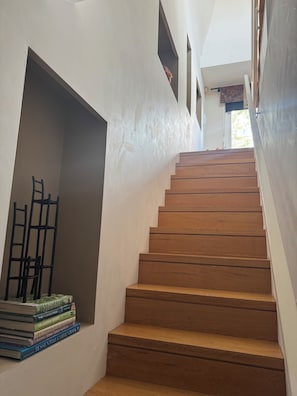 Eine Treppe mit hölzernen Stufen, die nach oben führen, ein Bücherstapel auf der linken Seite und ein Stuhl, der an der Wand lehnt.