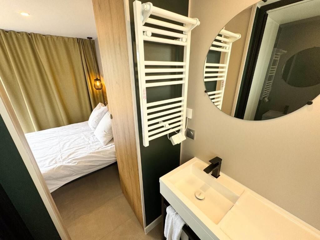 A hotel room with a bed, a white sink, a towel rack, and a mirror.