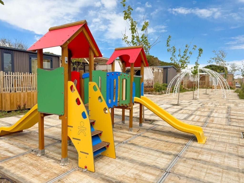 A playground with a yellow slide, a climbing structure, and a red-roofed playhouse.