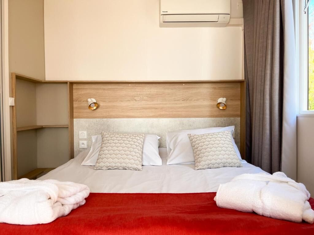 Een hotelkamer met een bed, een rode deken, twee kussens, een houten hoofdbord en een airconditioner.