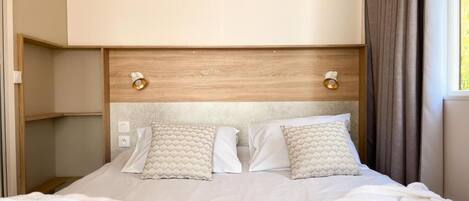 Een hotelkamer met een bed, een rode deken, twee kussens, een houten hoofdbord en een airconditioner.