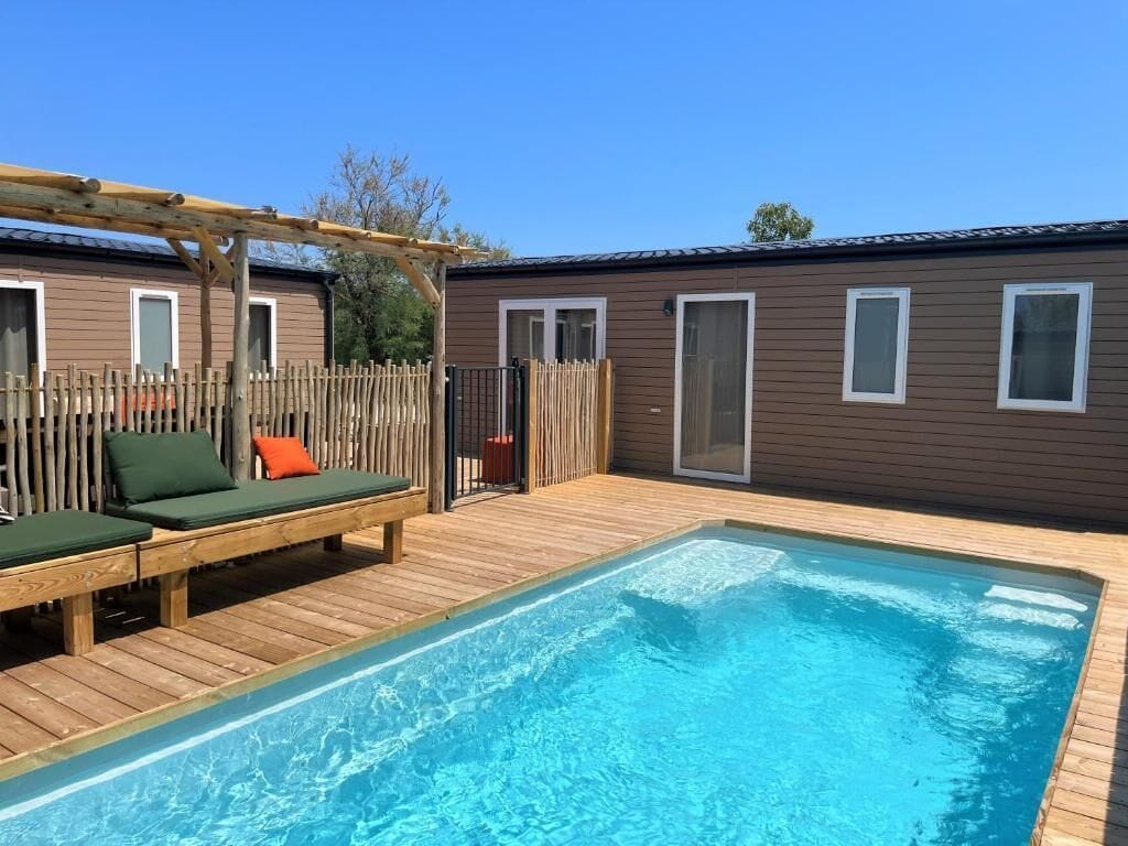 A swimming pool with wooden deck, lounge chairs, and a pergola.