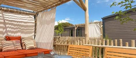 An outdoor dining area with a wooden table set for a meal, a wooden bench, and a covered seating area with cushions.