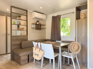 A compact room with a sofa, a dining table, and chairs. There is a basket, a tote bag, and a straw hat on the table. - La Clape Village  (Agde)