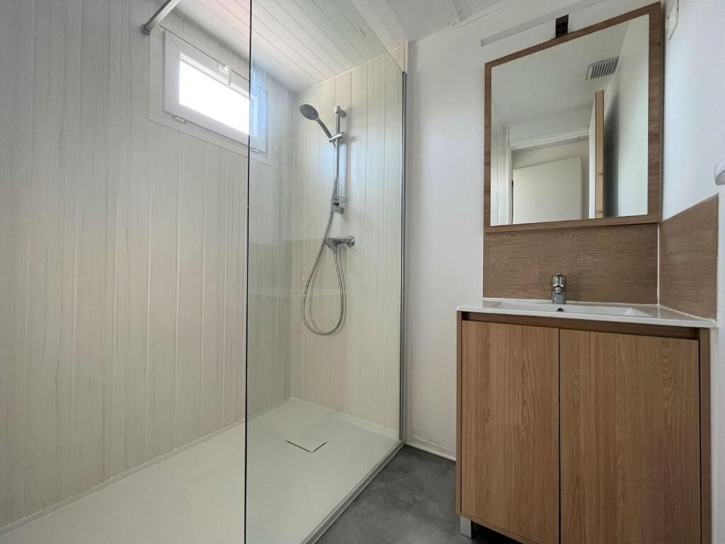 A modern bathroom with a glass shower enclosure, a wooden vanity, and a large mirror.