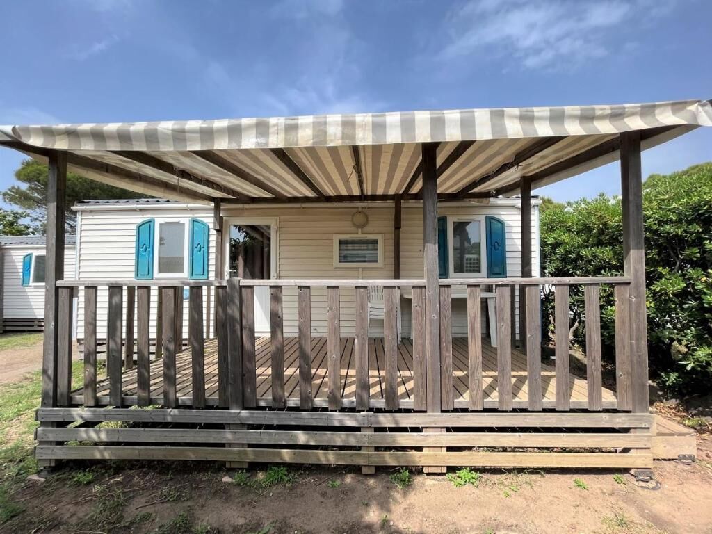 A mobile home with a wooden deck, a striped awning, and a small porch.