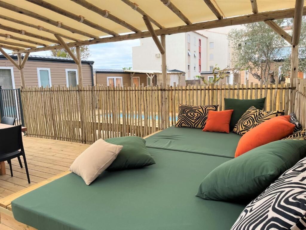 A covered outdoor seating area with a wooden deck, a pool, and a view of residential buildings.