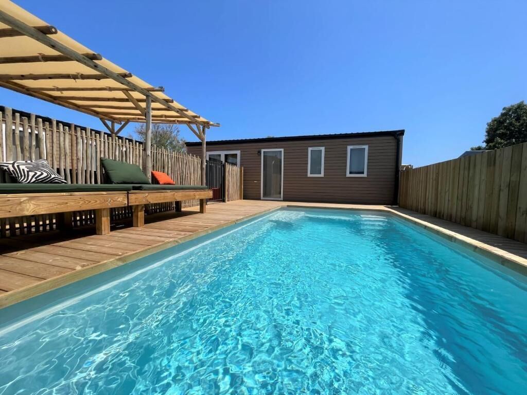 Une piscine avec une terrasse en bois et un espace salon couvert.