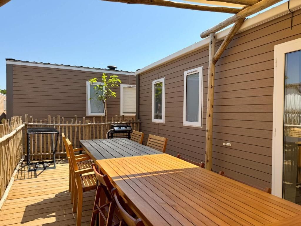 Une terrasse en bois avec une table et des chaises, un barbecue et un espace délimité par une clôture.