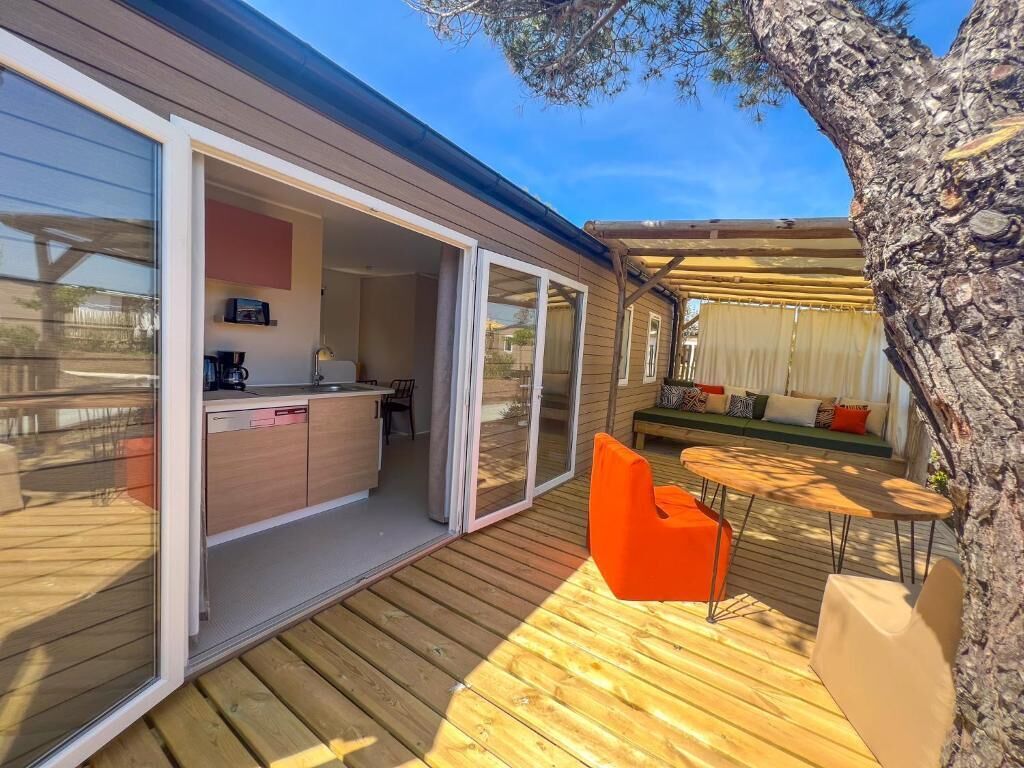 Un espacio abierto que incluye sala de estar, cocina, puertas de cristal correderas y una terraza con mobiliario exterior.