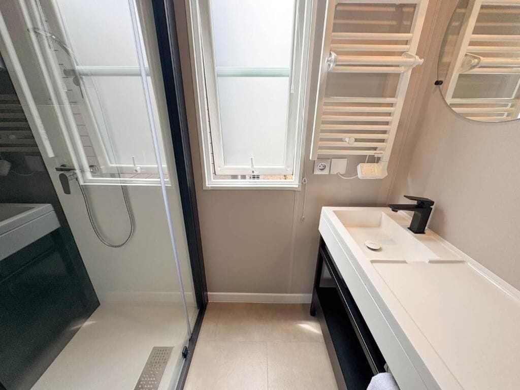 A bathroom with a shower, a sink, and a window.