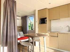 Habitación compacta con cama, una pequeña kitchenette, una mesa de comedor con sillas y una ventana con cortinas.