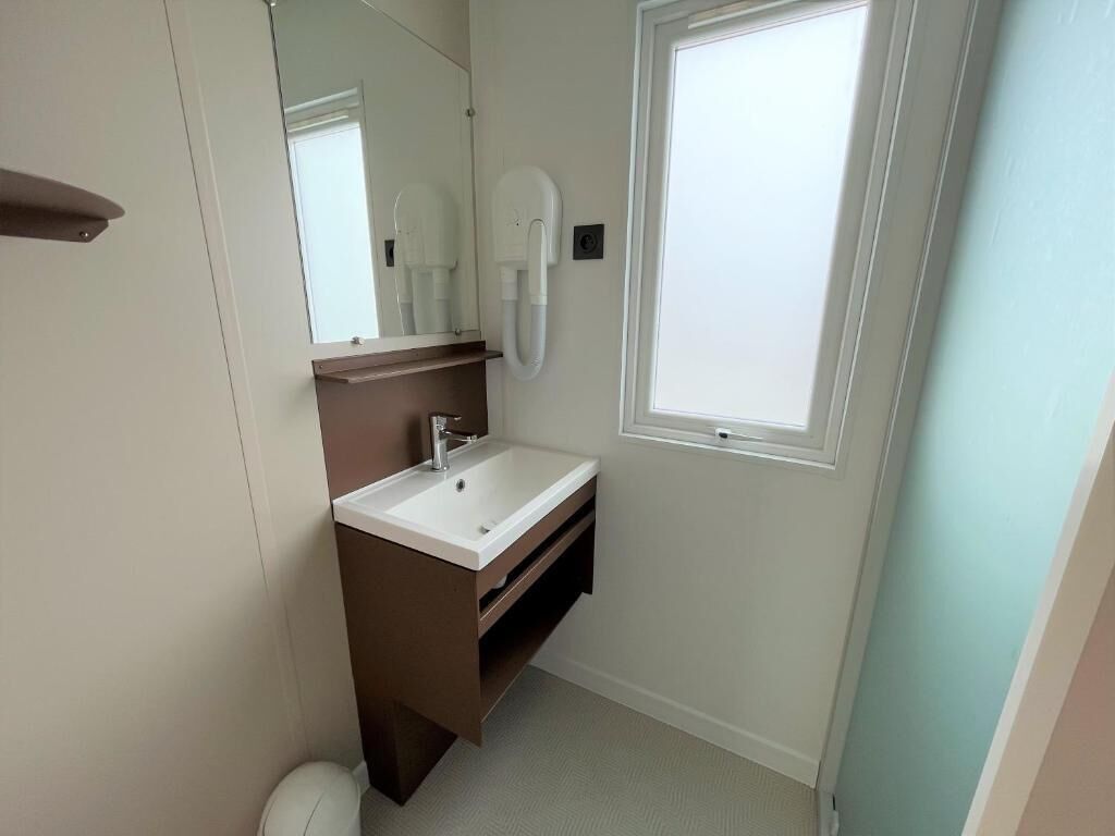 A bathroom with a white sink, a mirror, a towel rack, and a window.