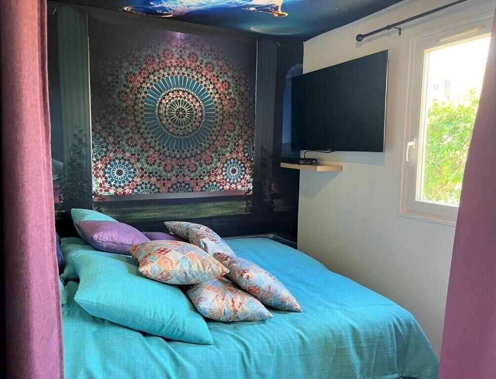 A bed with a patterned headboard, a television on the wall, and a window with daylight.