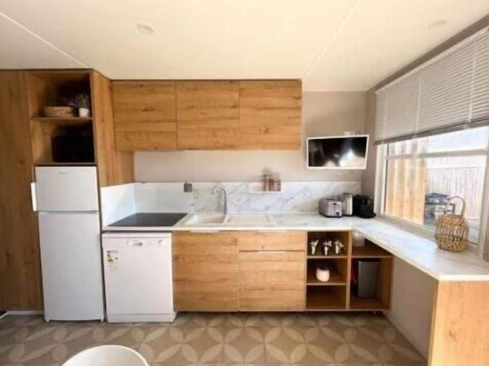 Een compacte keuken met houten kastjes, een ingebouwde gootsteen en een raam dat voor natuurlijk licht zorgt.