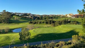 Un campo de golf con un estanque, árboles y una zona residencial al fondo.
