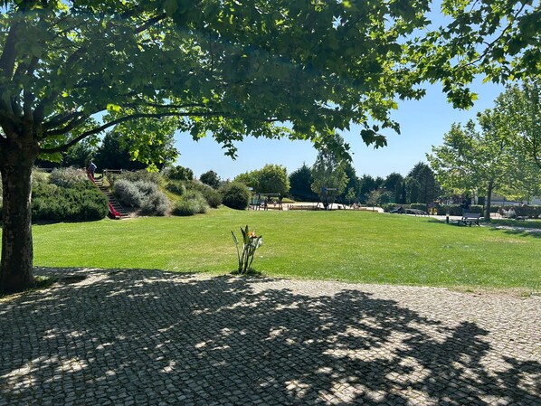 A paved area with a tree and grass, a playground with swings, and a bench.