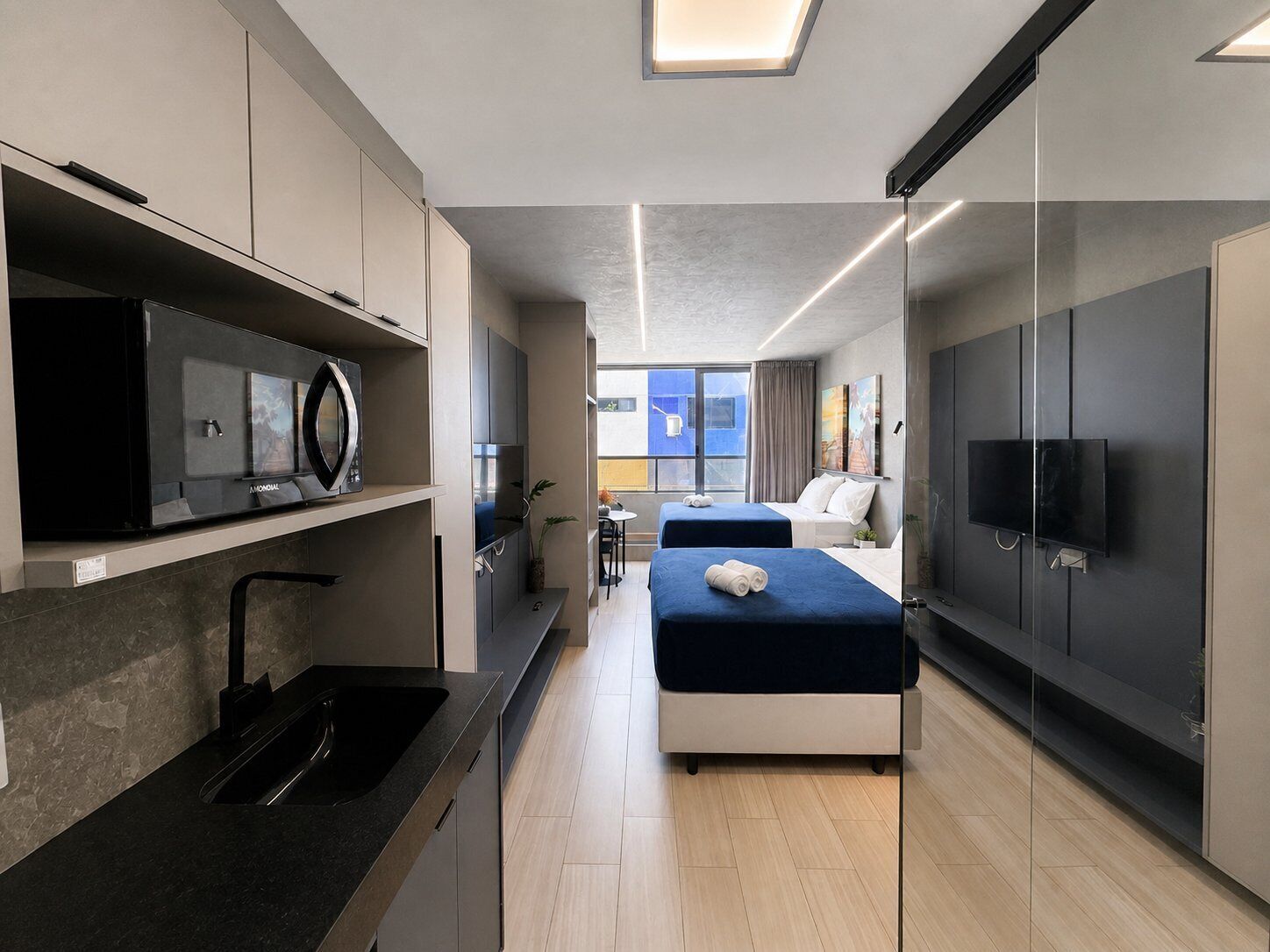 Habitación de hotel moderna con cocina, dos camas, un televisor y un ventanal grande.