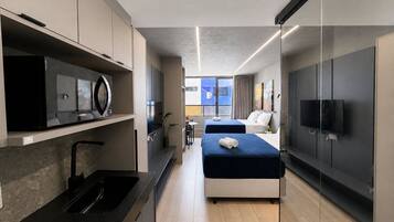 Habitación de hotel moderna con cocina, dos camas, un televisor y un ventanal grande.
