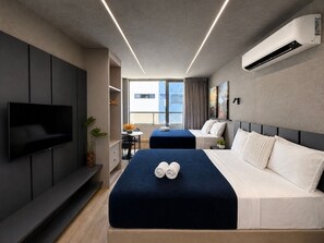 Quarto de hotel moderno com televisão de tela plana, duas camas, uma escrivaninha e uma janela grande.