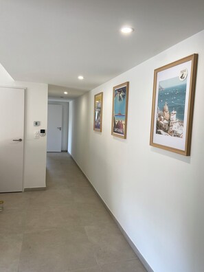 A hallway with white walls, a tiled floor, and three framed pictures depicting coastal scenes. - Two-bedroom apartment with garage, 200 meters from the beach, 3-star rating (Fréjus)