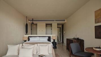 Habitación de hotel con cama, lámparas de noche, una silla, una mesita y vistas al pasillo.