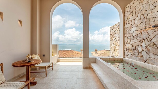Un balcón con pared de piedra, una piscina con pétalos rojos y vista al mar.