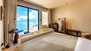 Habitación de hotel con una cama grande, un escritorio, un banco, un armario y vistas al mar.