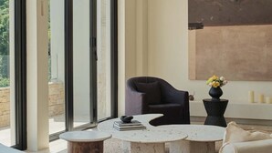 Un interior moderno con un amplio ventanal de arco, una mesa redonda, un sillón oscuro y un sofá blanco.