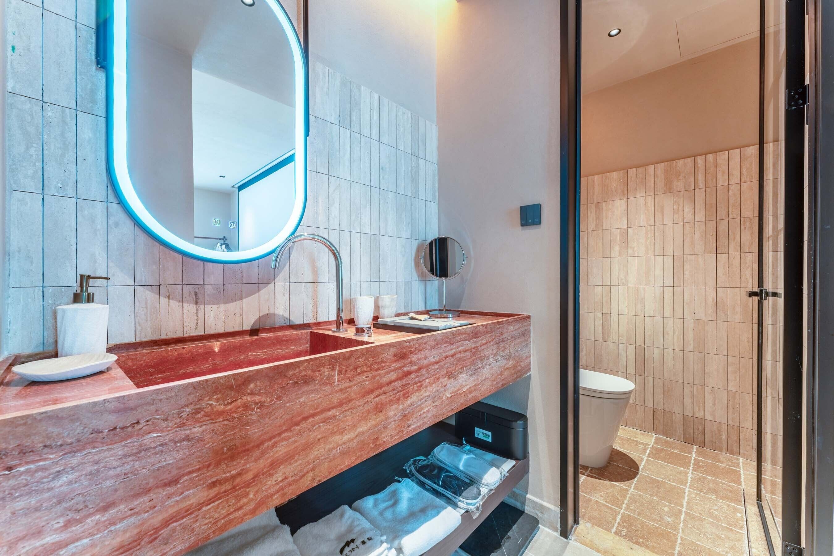 A modern bathroom with a marble vanity, a round mirror, a toilet, and a glass shower enclosure.