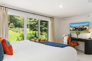 Ein Schlafzimmer mit einem großen Bett, einem Schreibtisch mit Stuhl, einem Fernseher und einem Fenster mit Vorhängen.