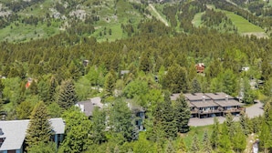 Una cabana de muntanya amb diversos edificis envoltada per un bosc dens i muntanyes.