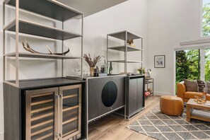 Ein modernes Wohnzimmer mit integrierter Küchenzeile, einer Couch, einem Couchtisch und Blick ins Grüne.