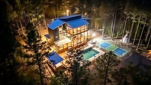 Una casa moderna de dos pisos con un amplio ventanal, piscina y cancha de tenis.