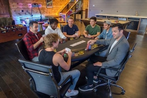 A group of people playing cards at a table in a room with a pool table, arcade machines, and a staircase. - Sleeps 52, Pond w/ Kayaks, Epic Game Room, Pool, UTV Access (Broken Bow)