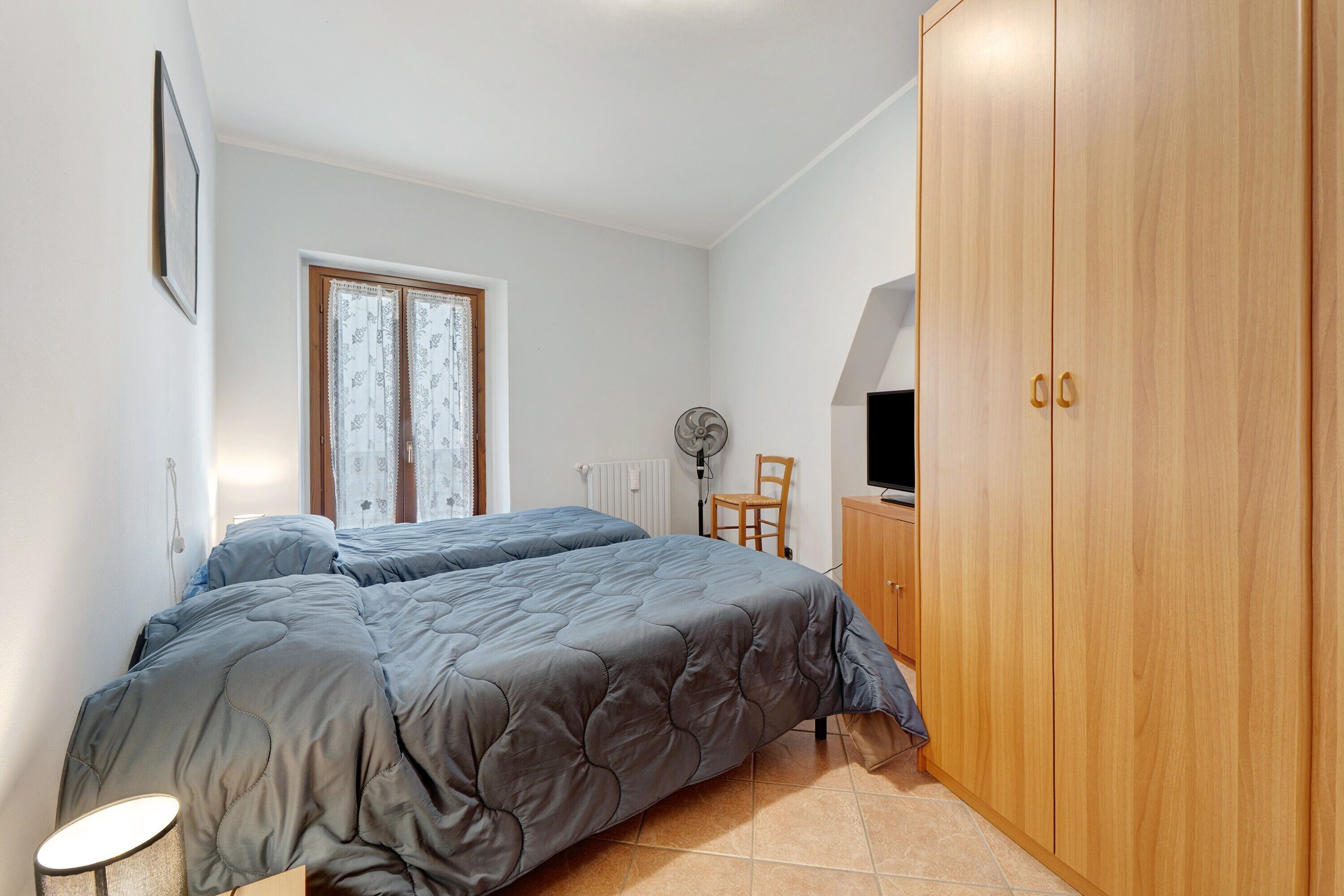 A bedroom with a bed, a wardrobe, a chair, a radiator, and a window.
