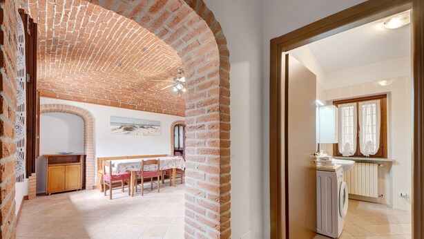 A room with a brick ceiling, a dining area with a table and chairs, and a washing machine. - Apartment 'Centenario Affittacamere' with Wi-Fi and Air Conditioning (Fara Novarese)