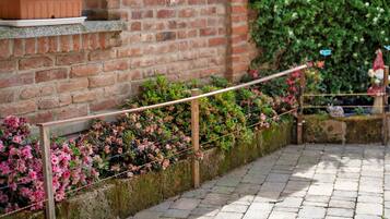 Un mur de briques avec une rambarde en bois, un chemin de pierres et des plantes en fleurs.